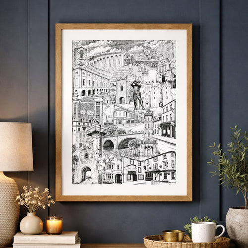 A framed black and white Alnwick Northumberland hangs on a dark navy paneled wall above a wooden console table styled with a lamp, books, a candle, and a potted plant. The print is enclosed in a light wood frame and displayed in a cozy living room setting.