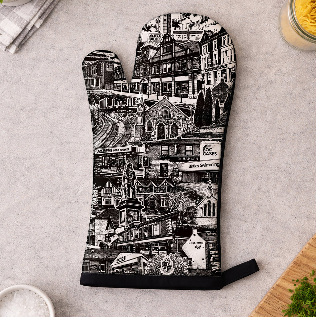 Oven mitt with black and white cityscape design on a kitchen counter.