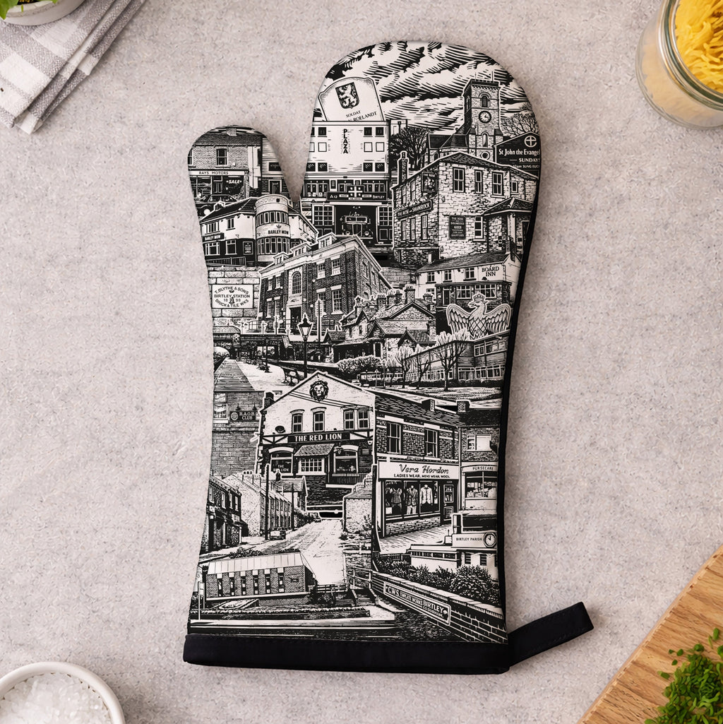 Oven mitt with black and white cityscape design on a kitchen counter.