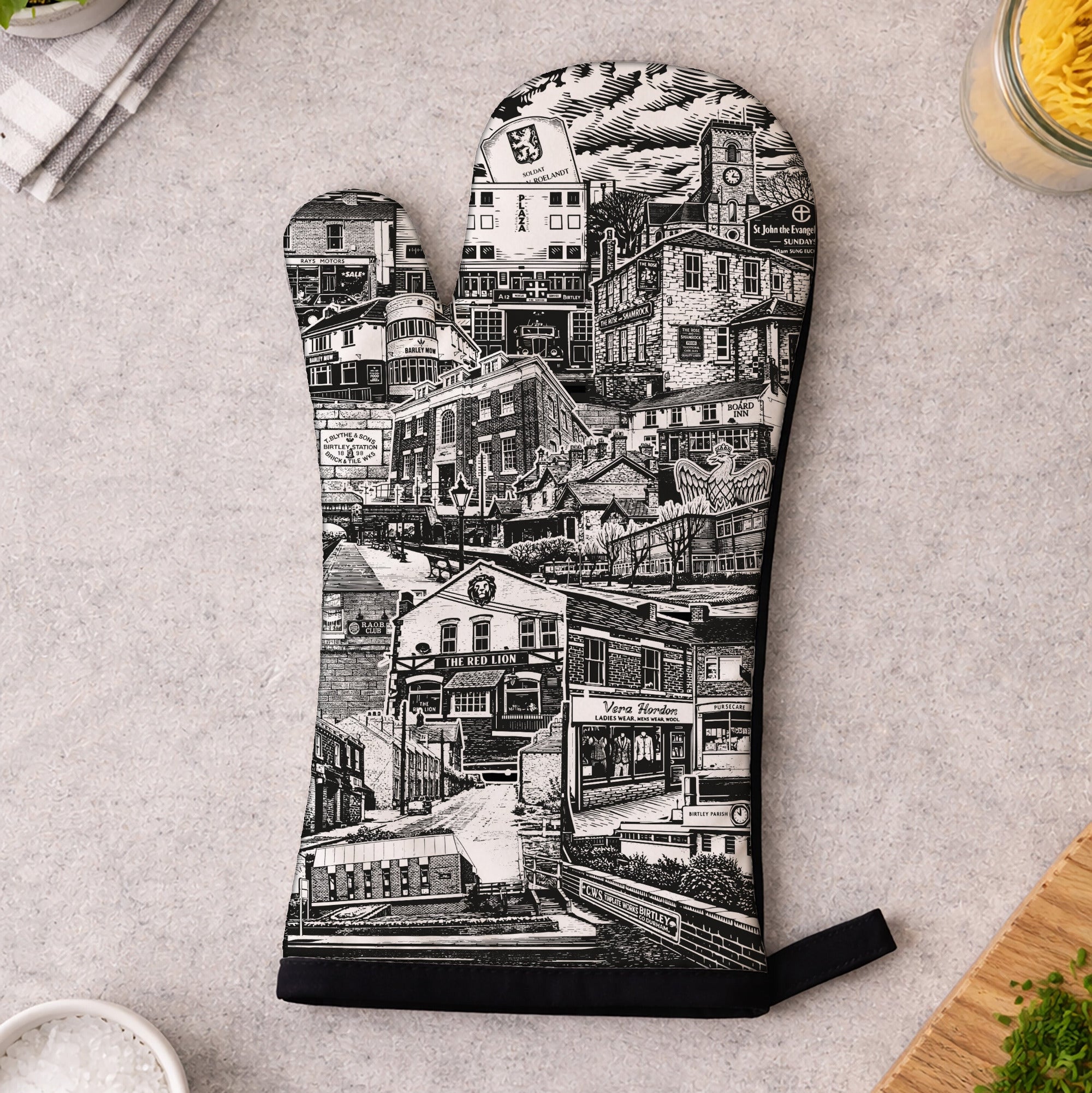 Oven mitt with black and white cityscape design on a kitchen counter.