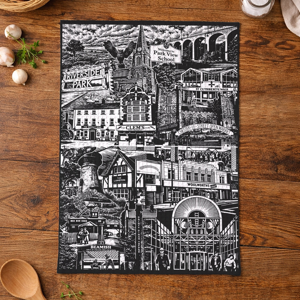 Black and white cityscape tea towel on a wooden table with kitchen items.