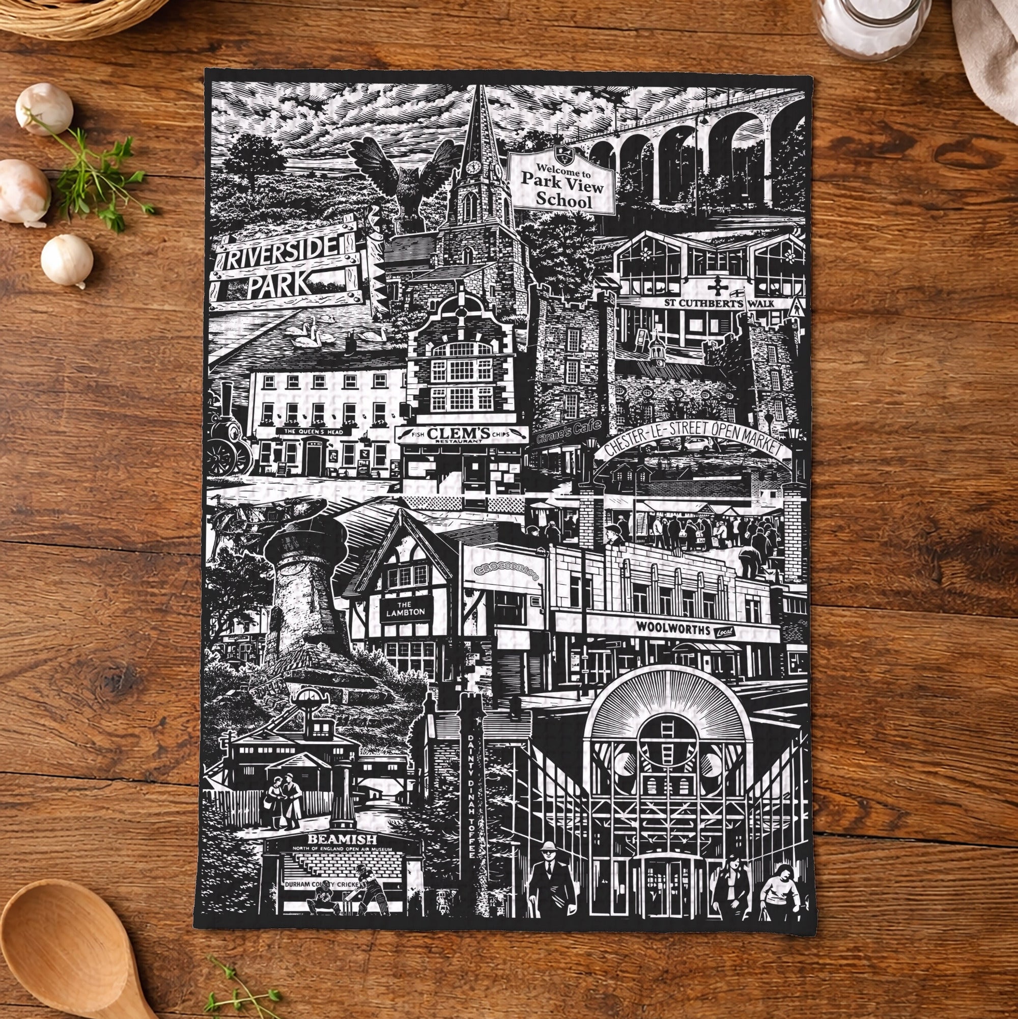 Black and white cityscape tea towel on a wooden table with kitchen items.