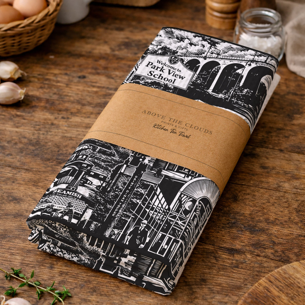 Folded fabric with black and white pattern and brown label on a wooden surface with kitchen items.