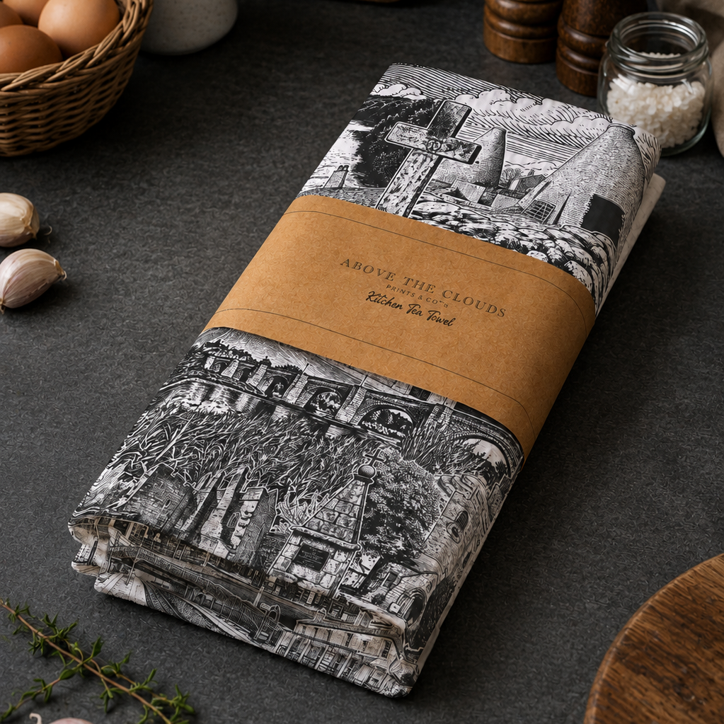 Folded tea towel with black and white design and brown label on a dark surface with kitchen items.