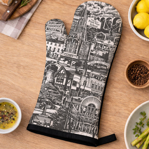 Oven glove with black and white pattern on a wooden table with food items.