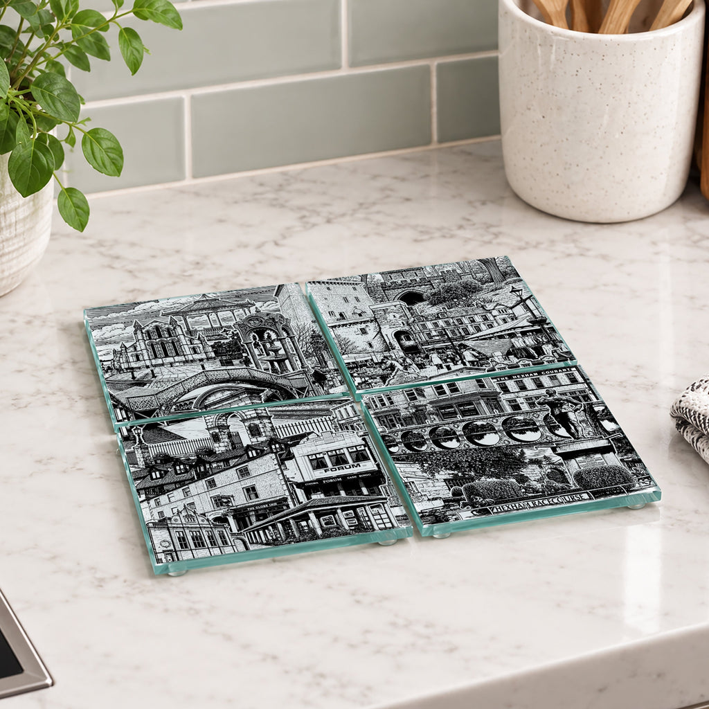 Four square glass coasters with a black and white city street scene print, arranged in a 2x2 grid on a white marble kitchen countertop.