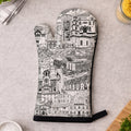 A single oven mitt laid flat on a light gray countertop, printed with a black-and-white illustrated cityscape and the word "HORBURY" near the bottom. Surrounding props include a small bowl of salt, chopped parsley, a wooden cutting board, and kitchen items in the corners.