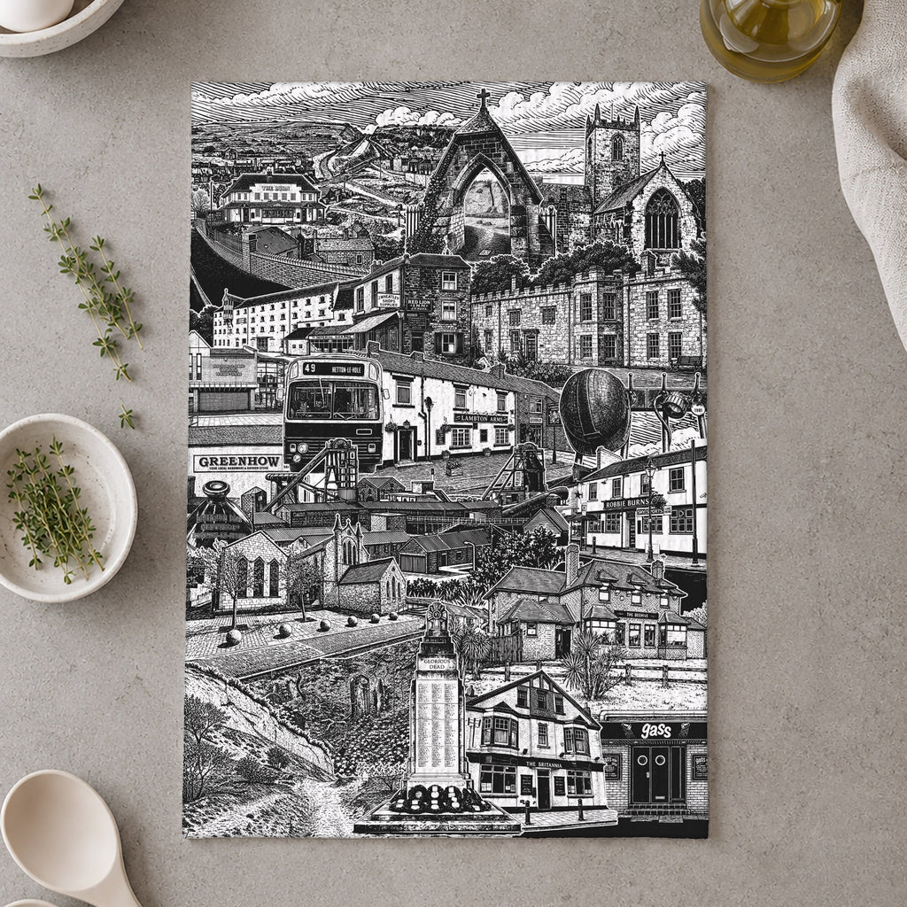 Tea towel with black and white cityscape design on a kitchen counter with utensils and plants.