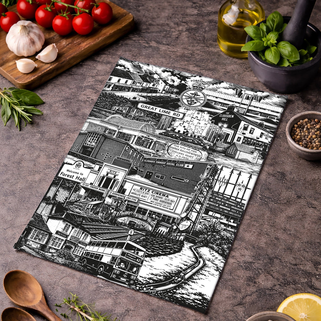Tea towel with black and white cityscape design on a wooden surface with ingredients.
