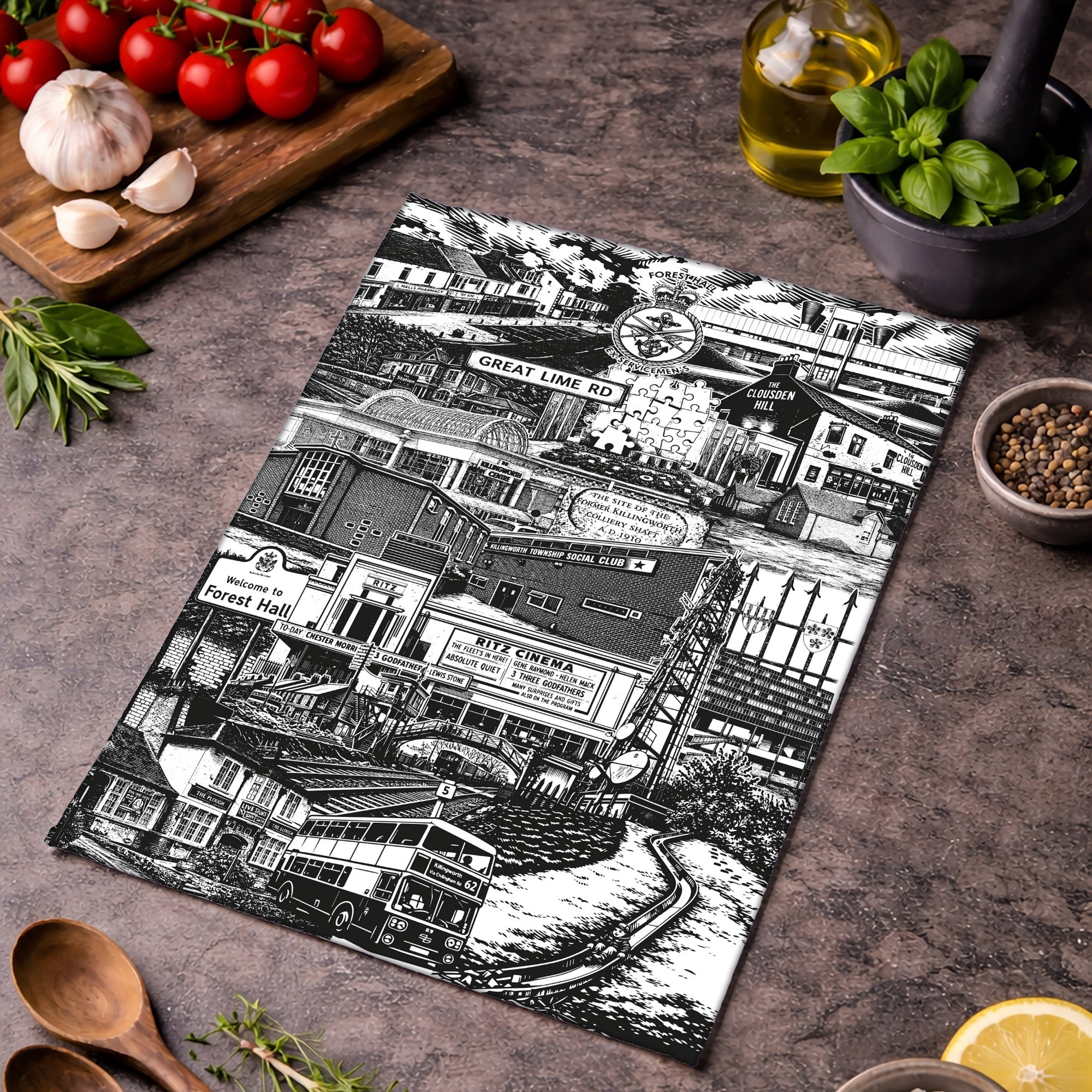 Tea towel with black and white cityscape design on a wooden surface with ingredients.
