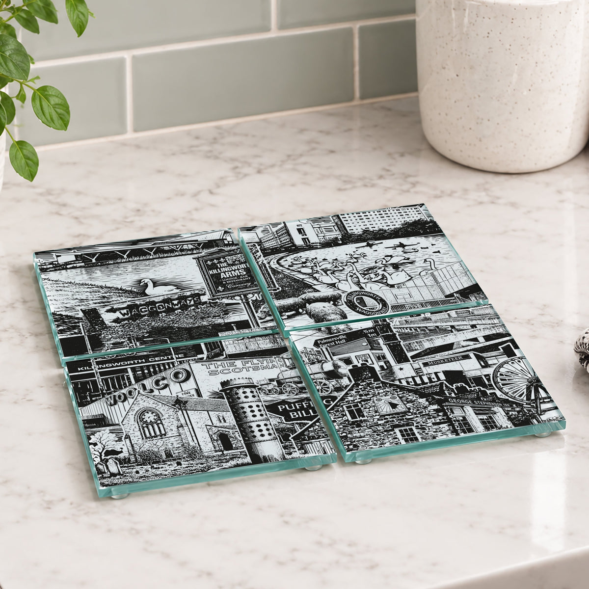 Four square glass coasters with a black and white industrial collage print of Killingworth, arranged on a white marble kitchen countertop.