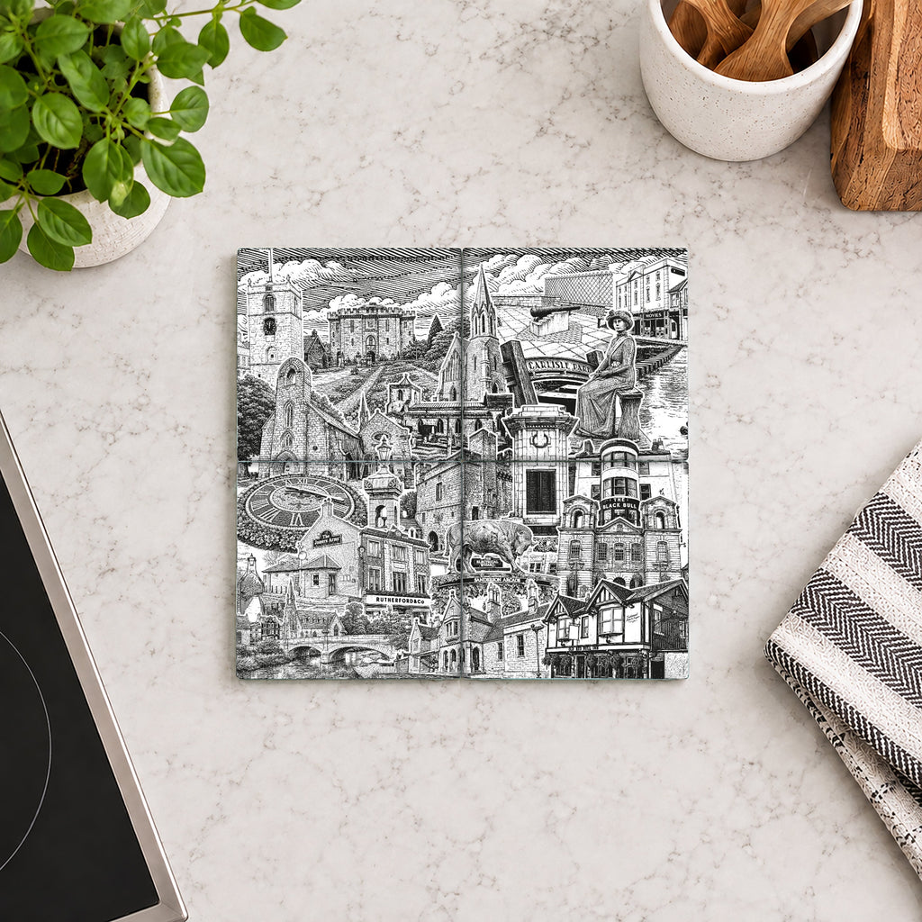 A square black and white illustrated coaster featuring a detailed collage-style drawing of architectural landmarks and figures, displayed on a light marble countertop with kitchen props.