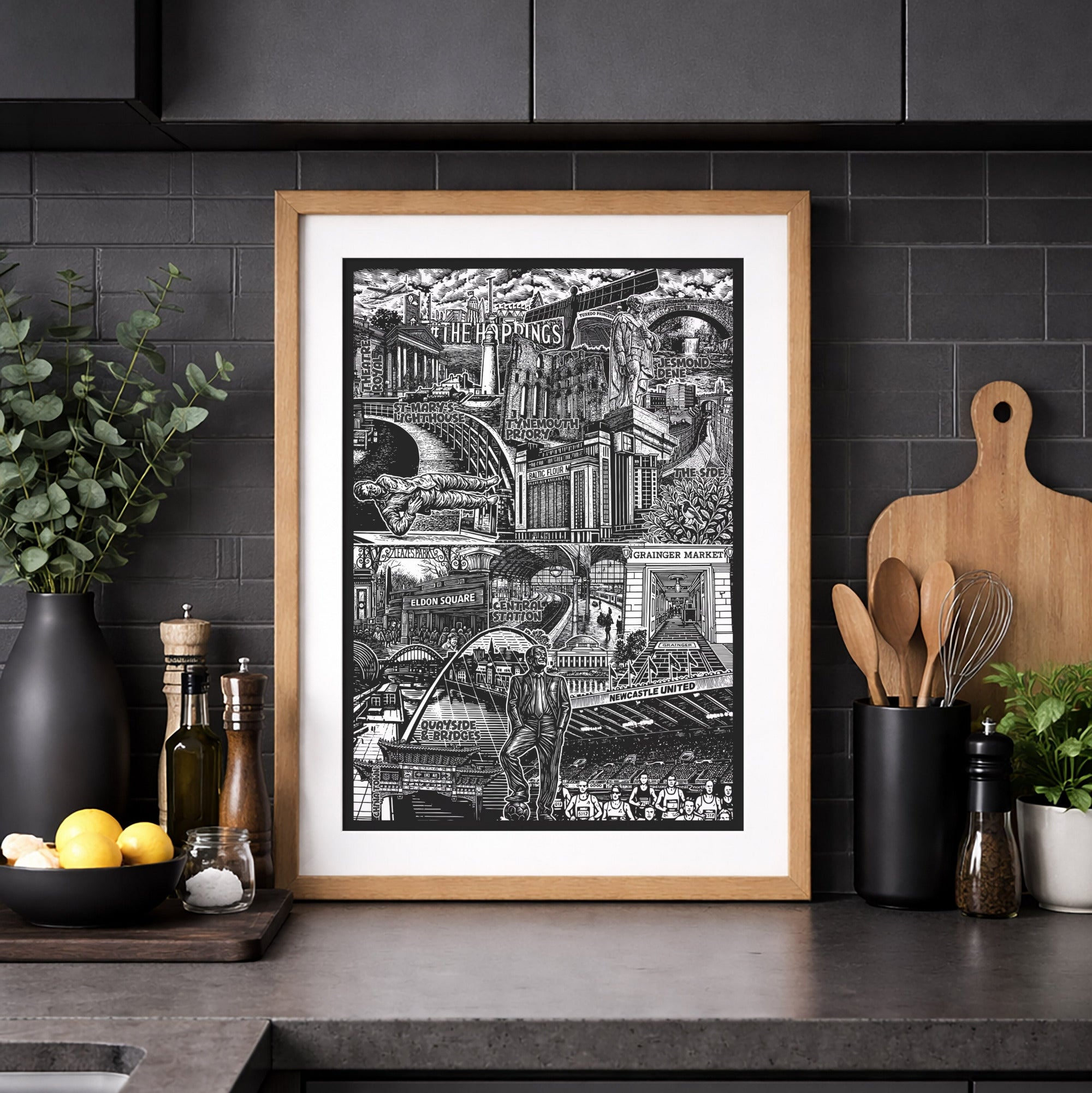 Framed black and white cityscape print on a kitchen counter with dark cabinets and decor.