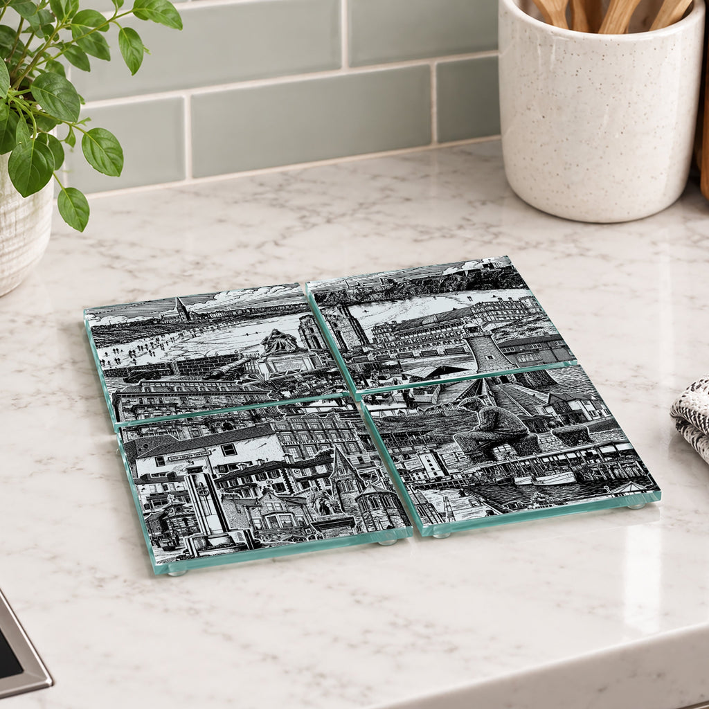 Four square glass coasters with a black and white architectural cityscape print, arranged on a white marble kitchen countertop.