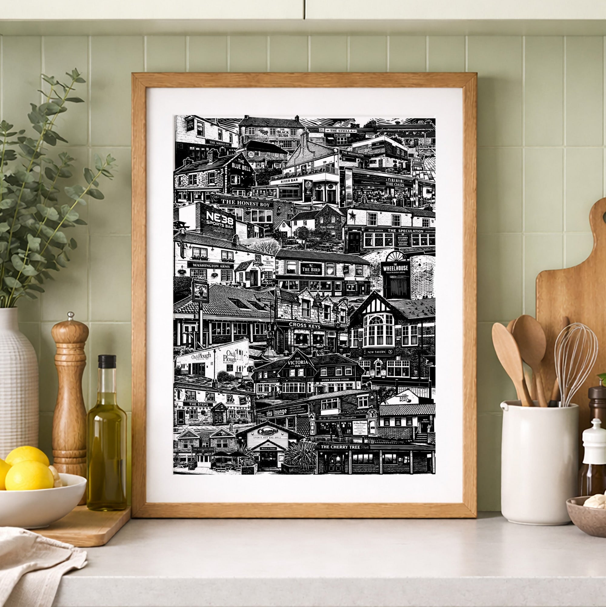 Framed black and white print on a kitchen counter with green cabinets and decor.