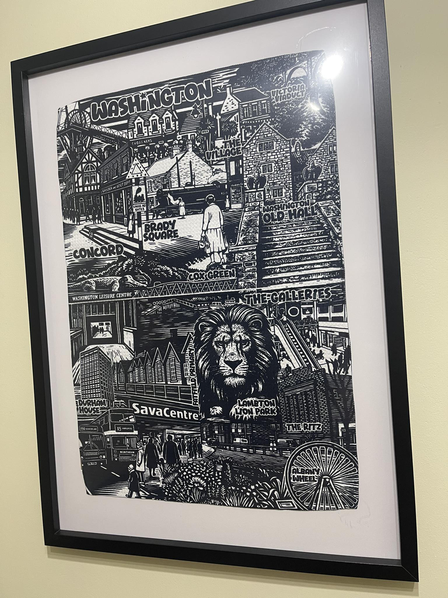 Framed black and white artwork of a cityscape with a lion's head in the center, displayed on a wall.