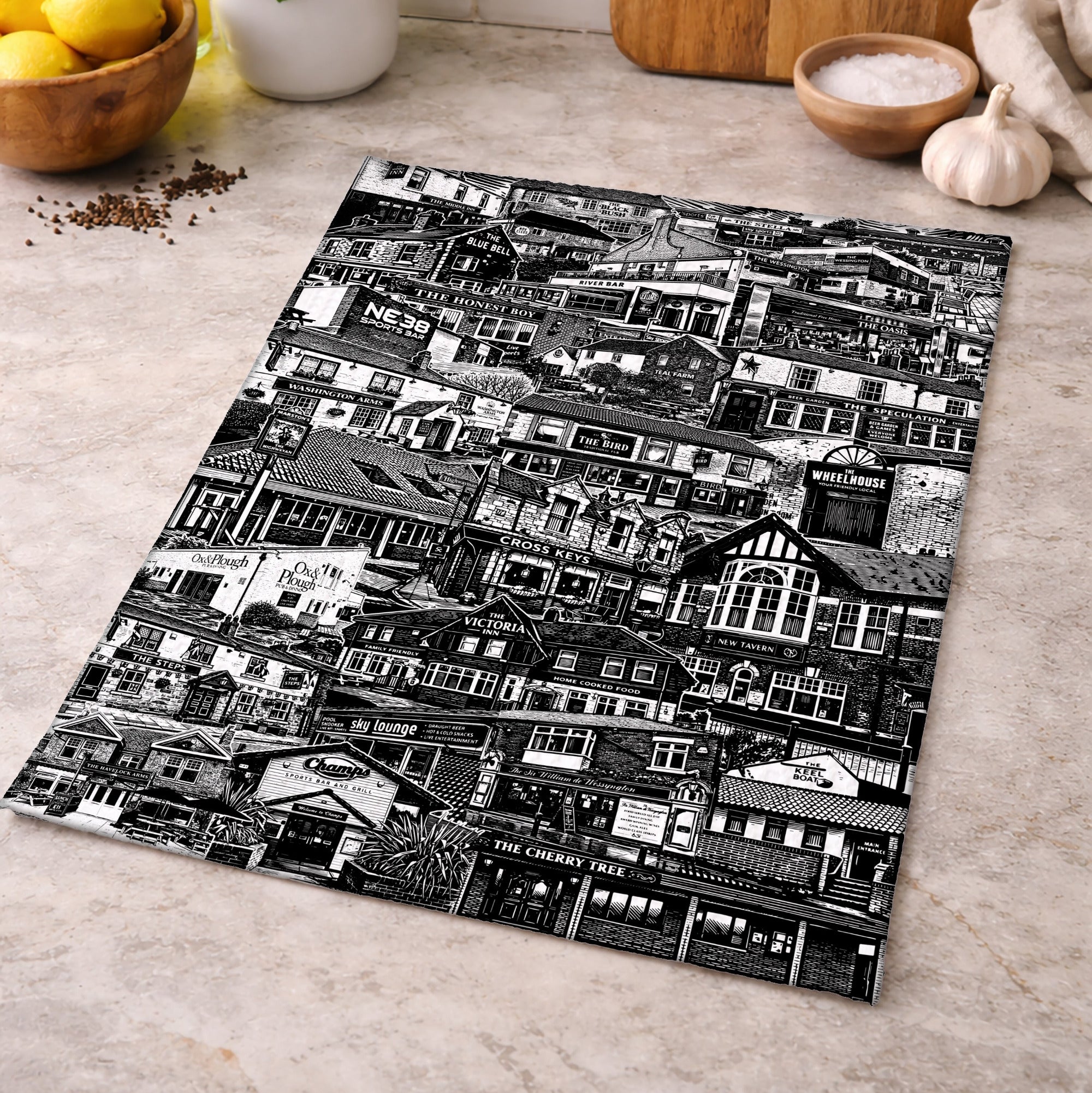 Black and white patterned cutting board on a kitchen counter with lemons and herbs in the background.