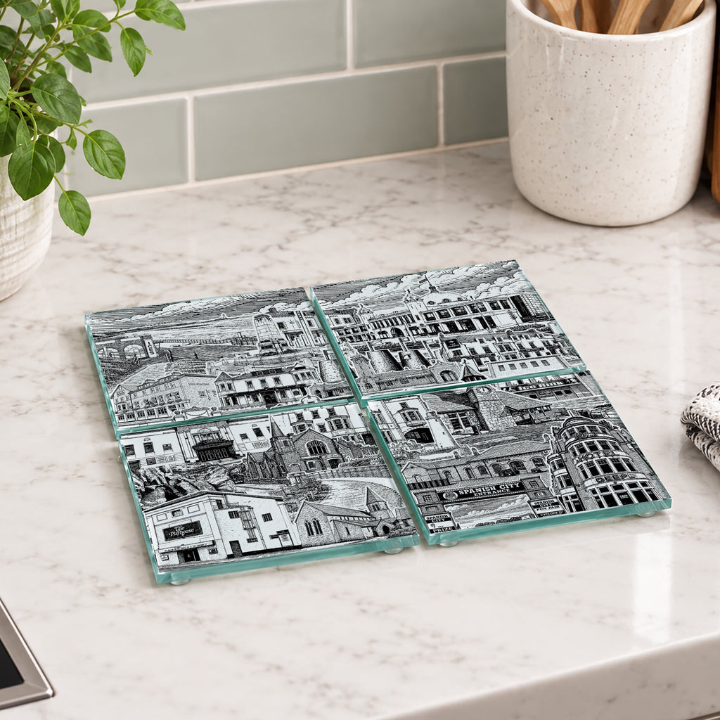 Four square glass coasters with a black and white architectural cityscape print, arranged on a white marble kitchen countertop.