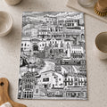 Black and white cityscape tea towel on a kitchen counter with utensils.